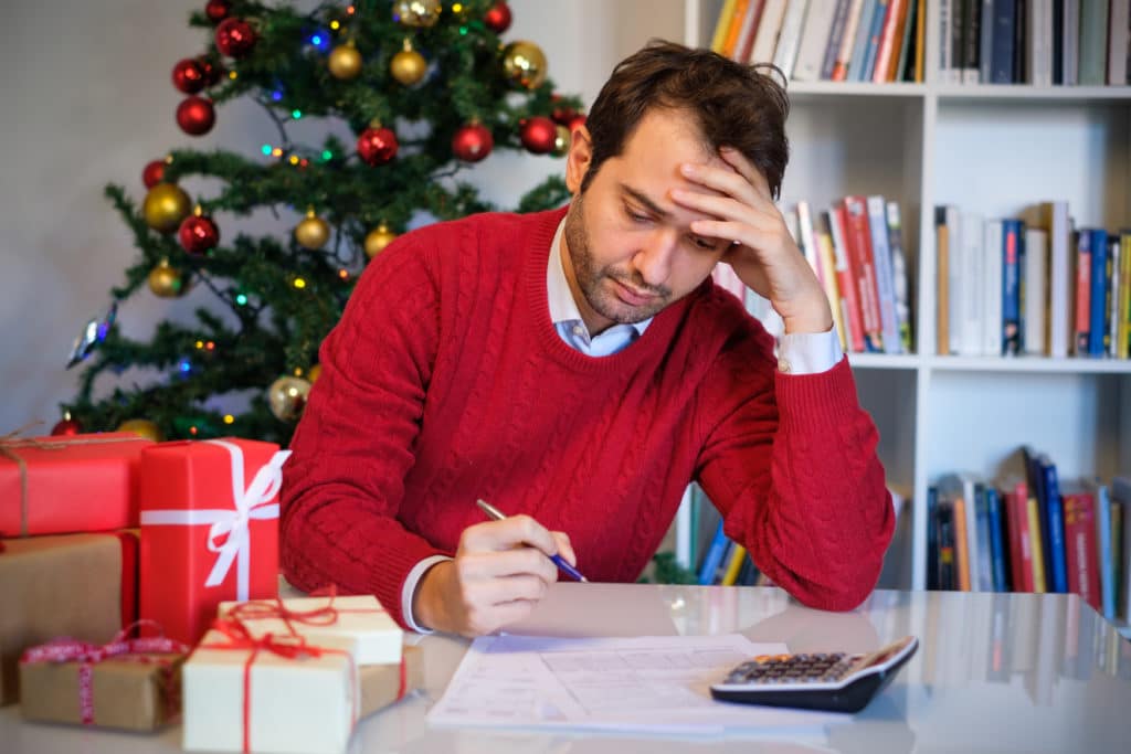 man uses pen and calculator gifts and tree in background