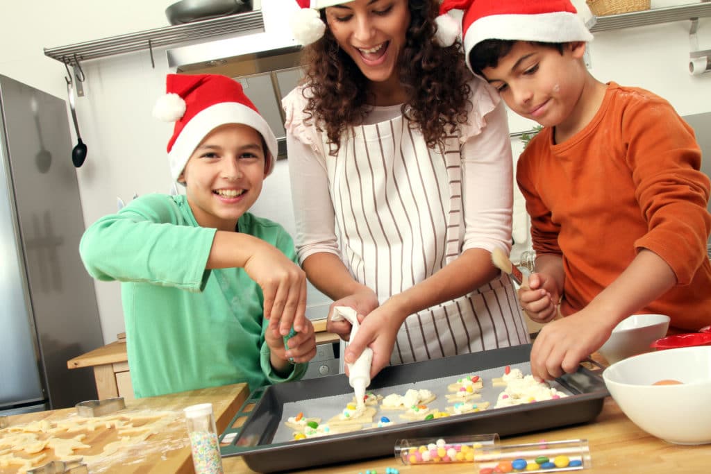 woman bakes holiday cookies with two boys